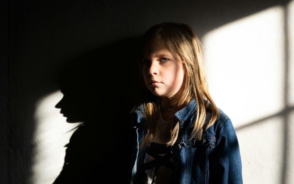 A girl in denim jacket with long hair stands with half her face in shadow