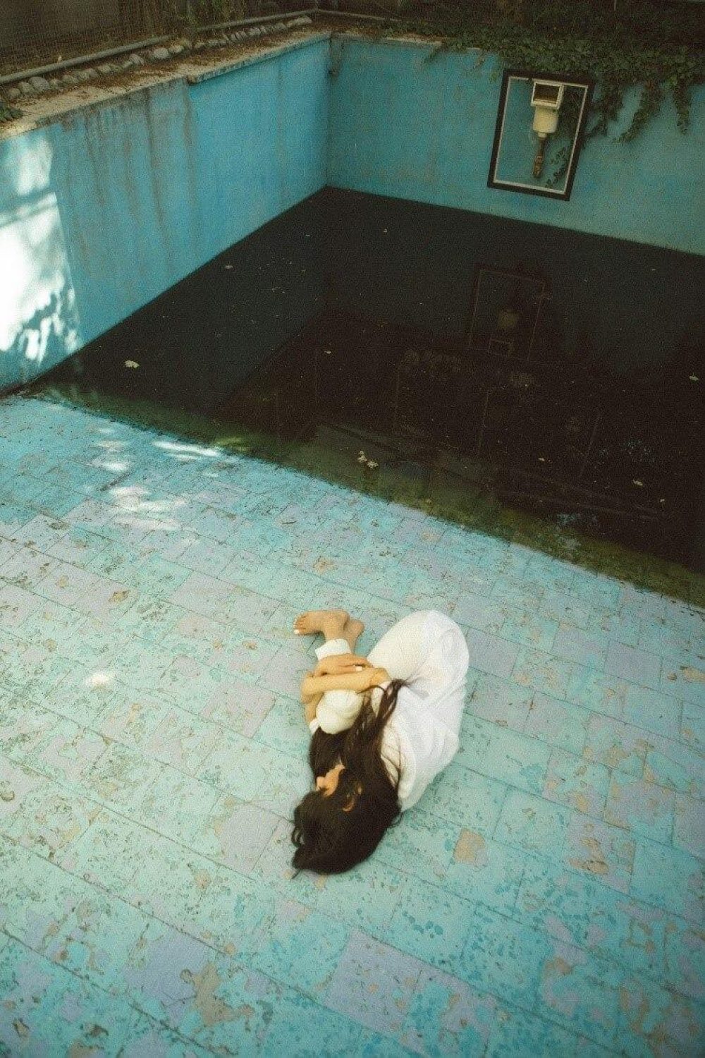 A girl dressed in white lies curled on the floor in the garden